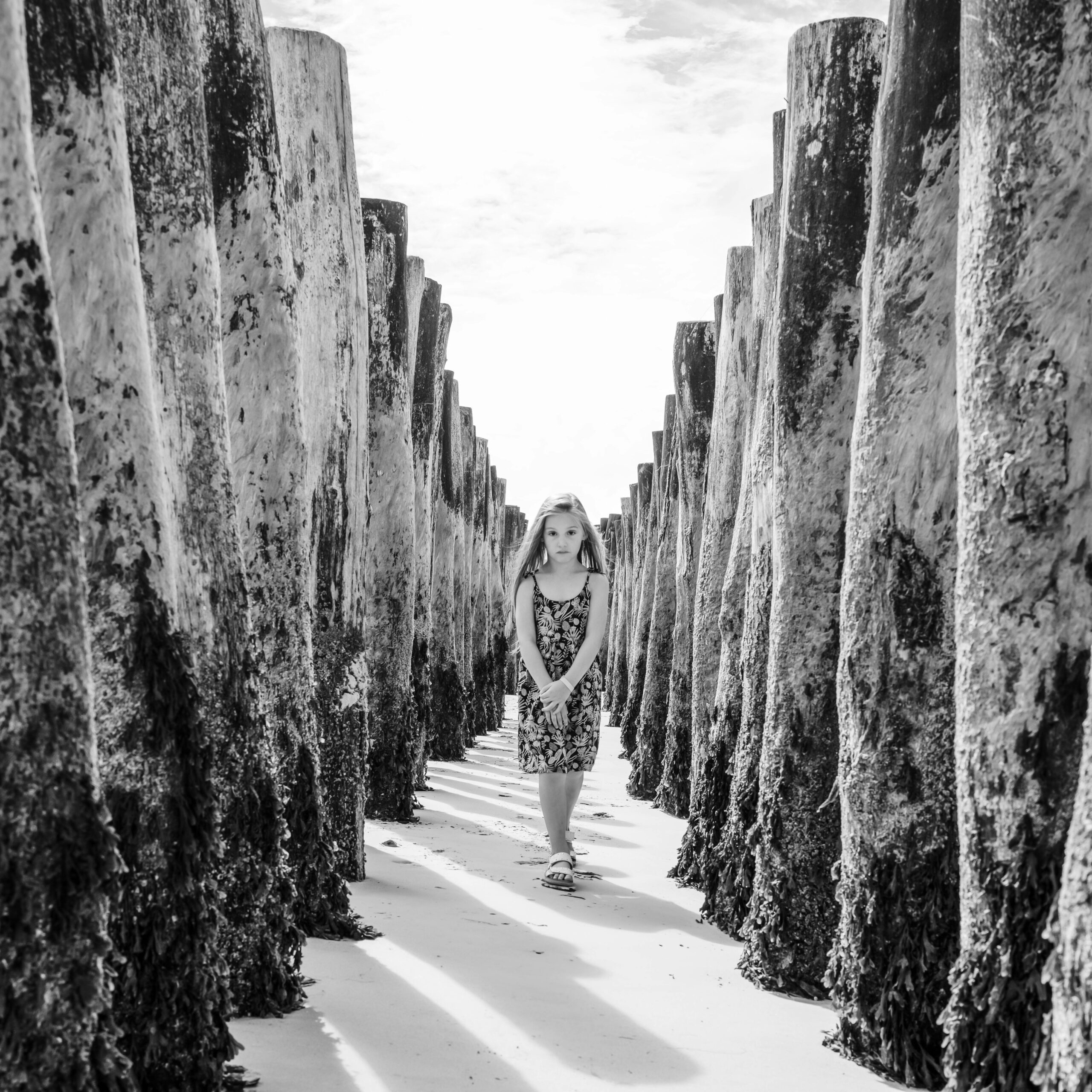 Une jeune fille marchant entre des rangées de poteaux en bois sur une plage.