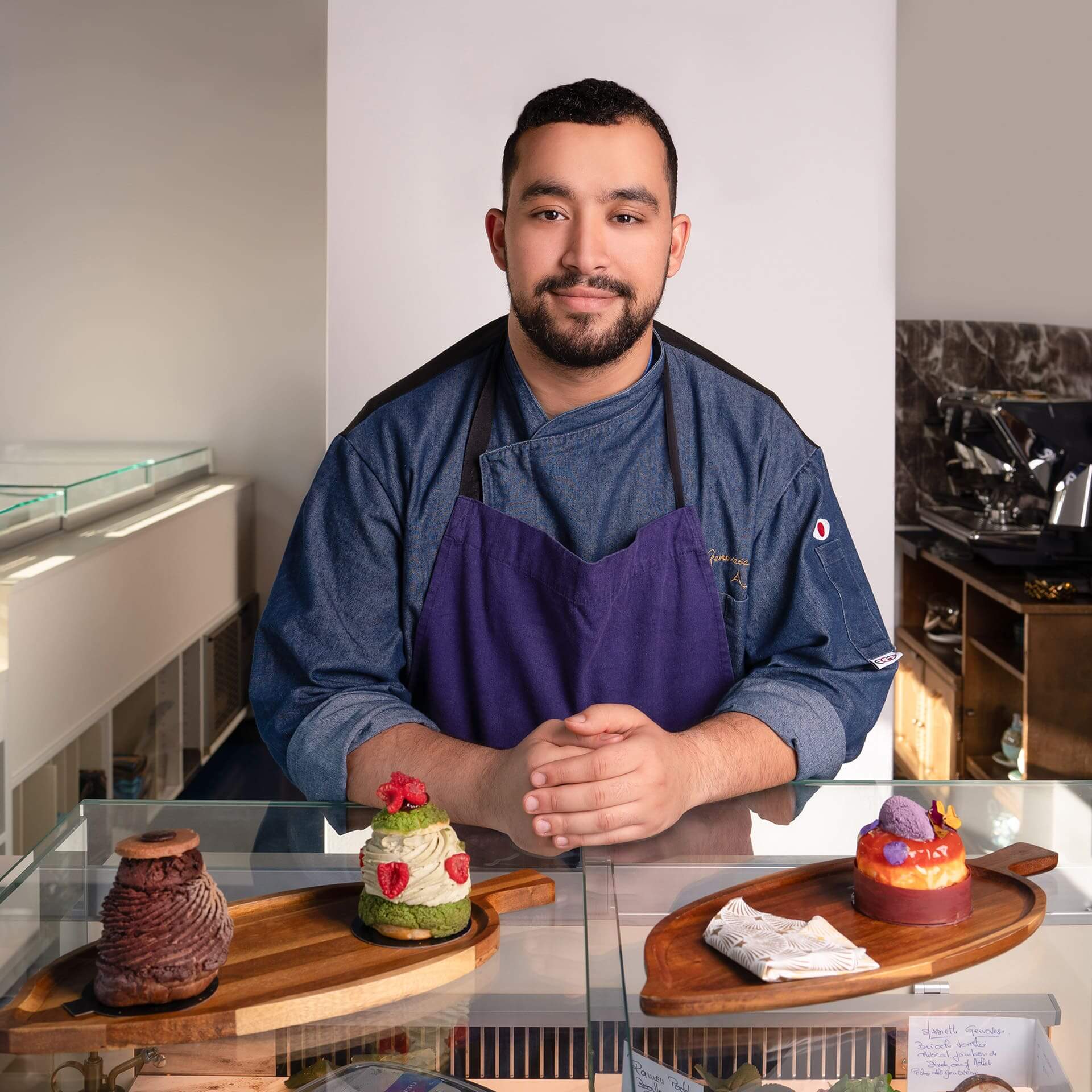 Un pâtissier souriant, debout derrière un comptoir, présentant des desserts.