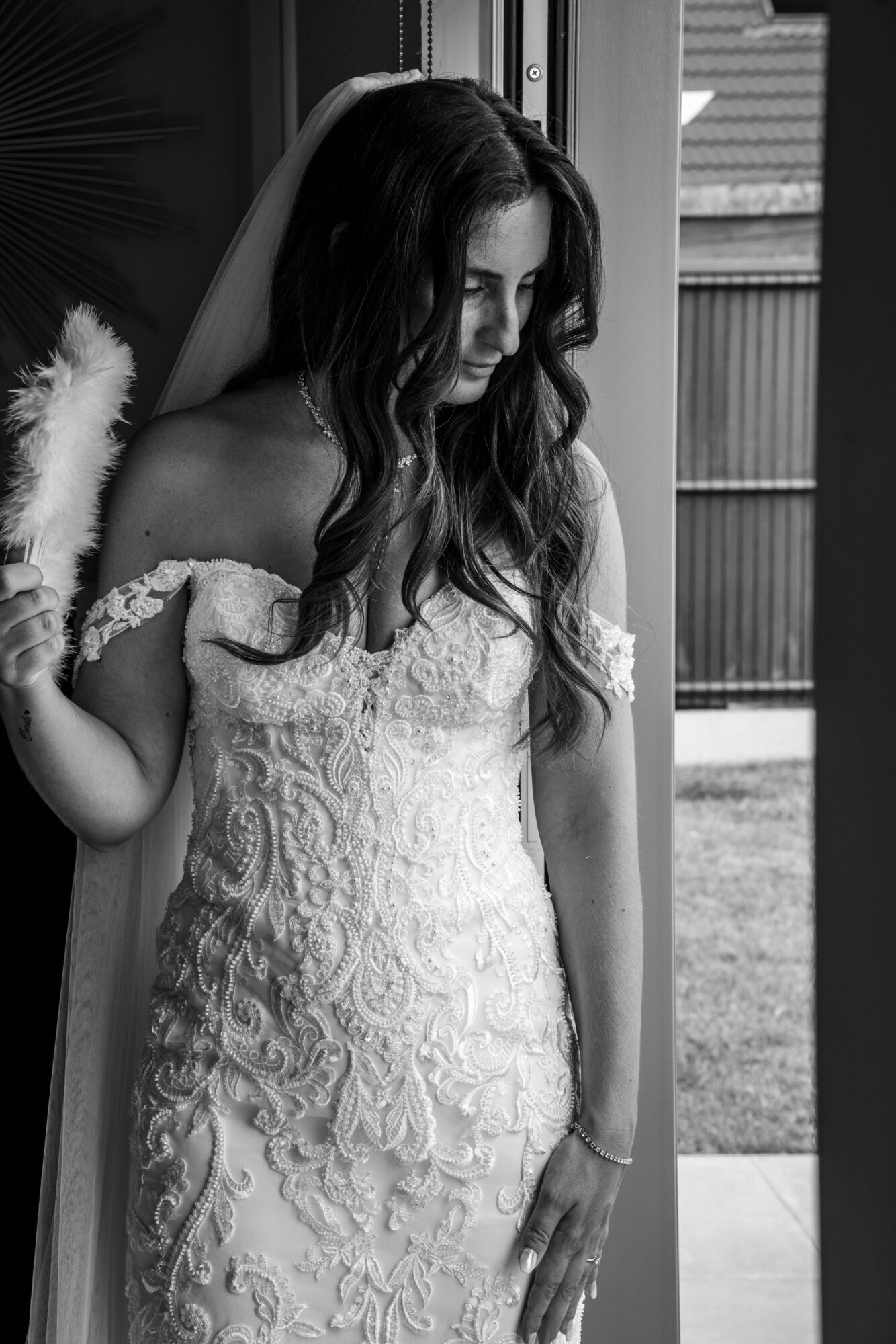 Portrait en noir et blanc d’une mariée en robe brodée près d’une fenêtre